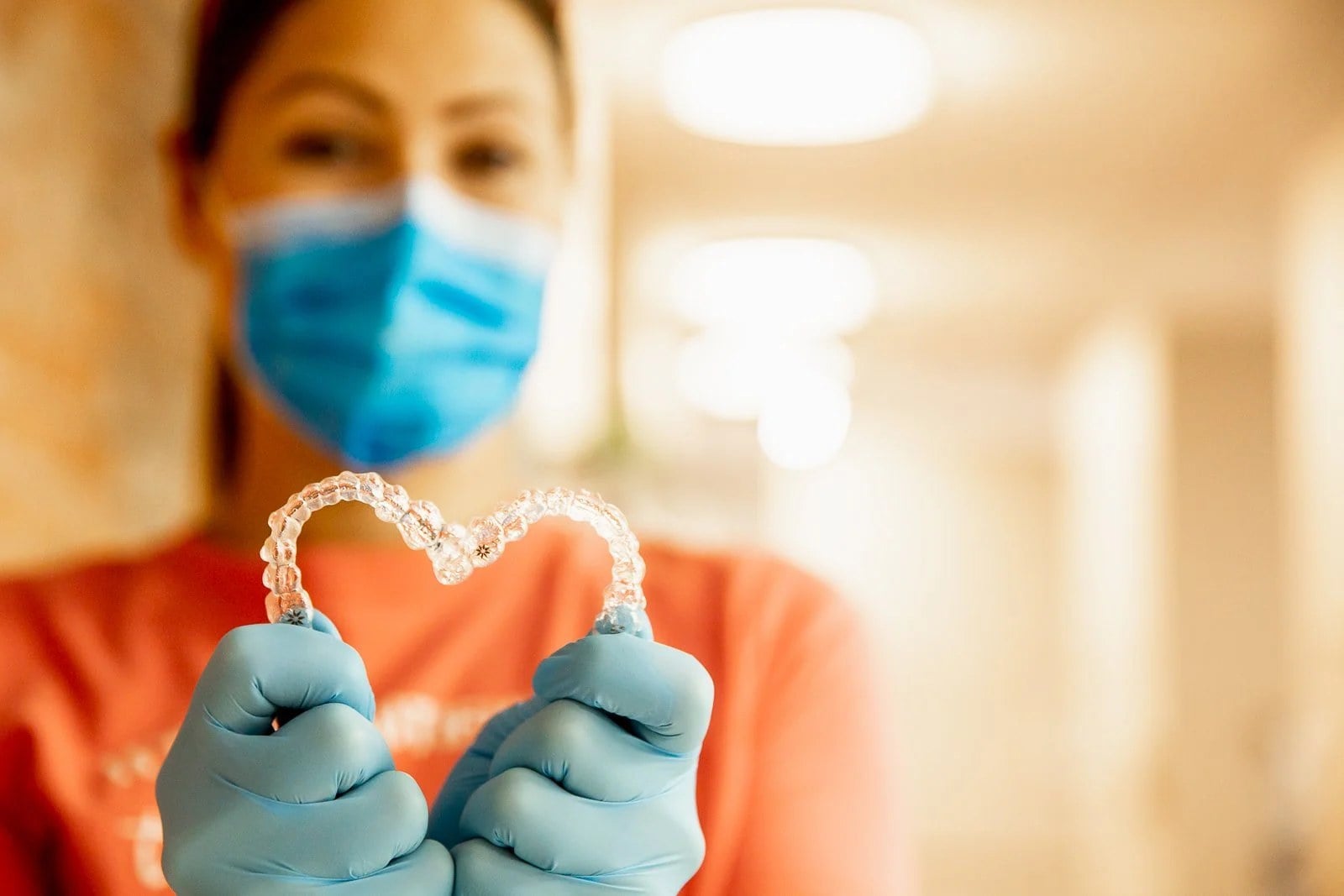 A dental team member in a mask holding up a pair of clear aligner trays