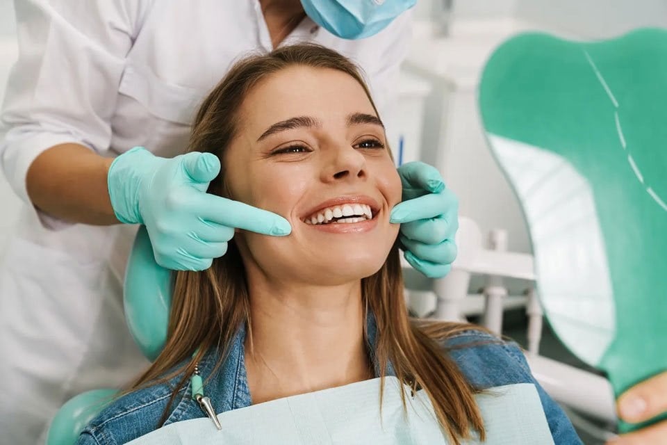 A smiling patient in a dental chair, with a gloved clinician beside her
