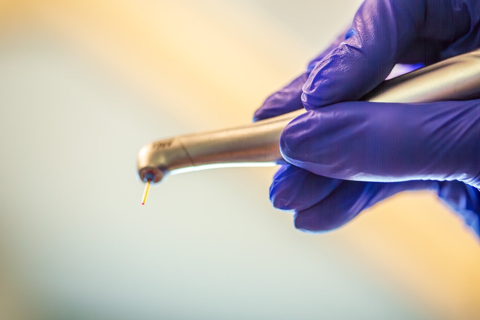 A gloved hand holding a dental laser handpiece