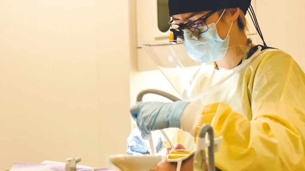 Clinician in PPE with loupes and face shield during a procedure
